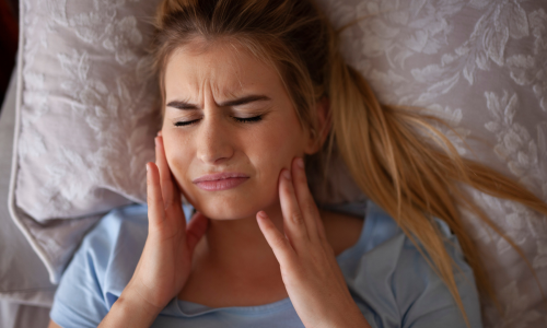 girl in bed holding jaw